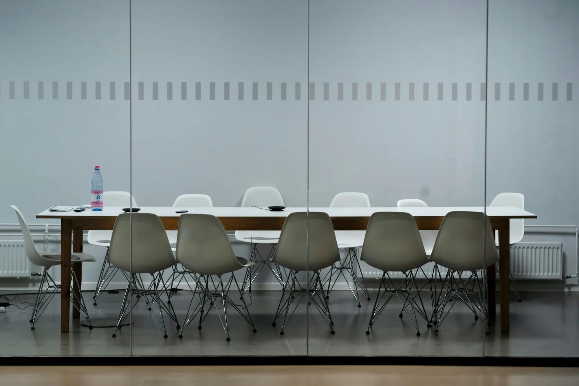 An empty meeting room with a long table and white chairs